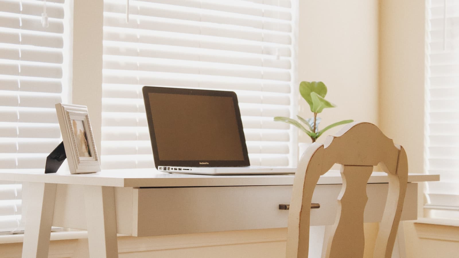 Laptop on a white desk by a window with blinds