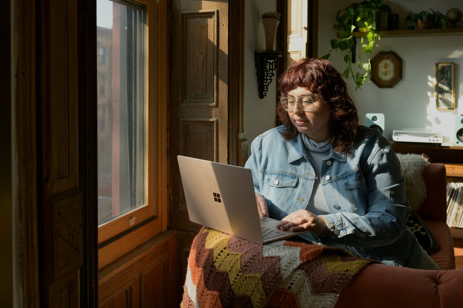 Person using a laptop on a sofa in a sunlit flat