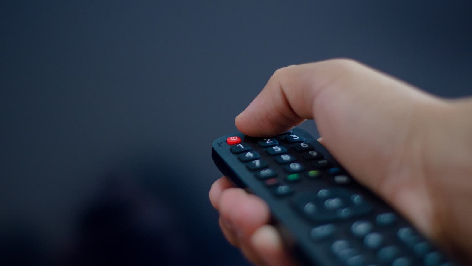 Hand holding a TV remote control pointed at a screen